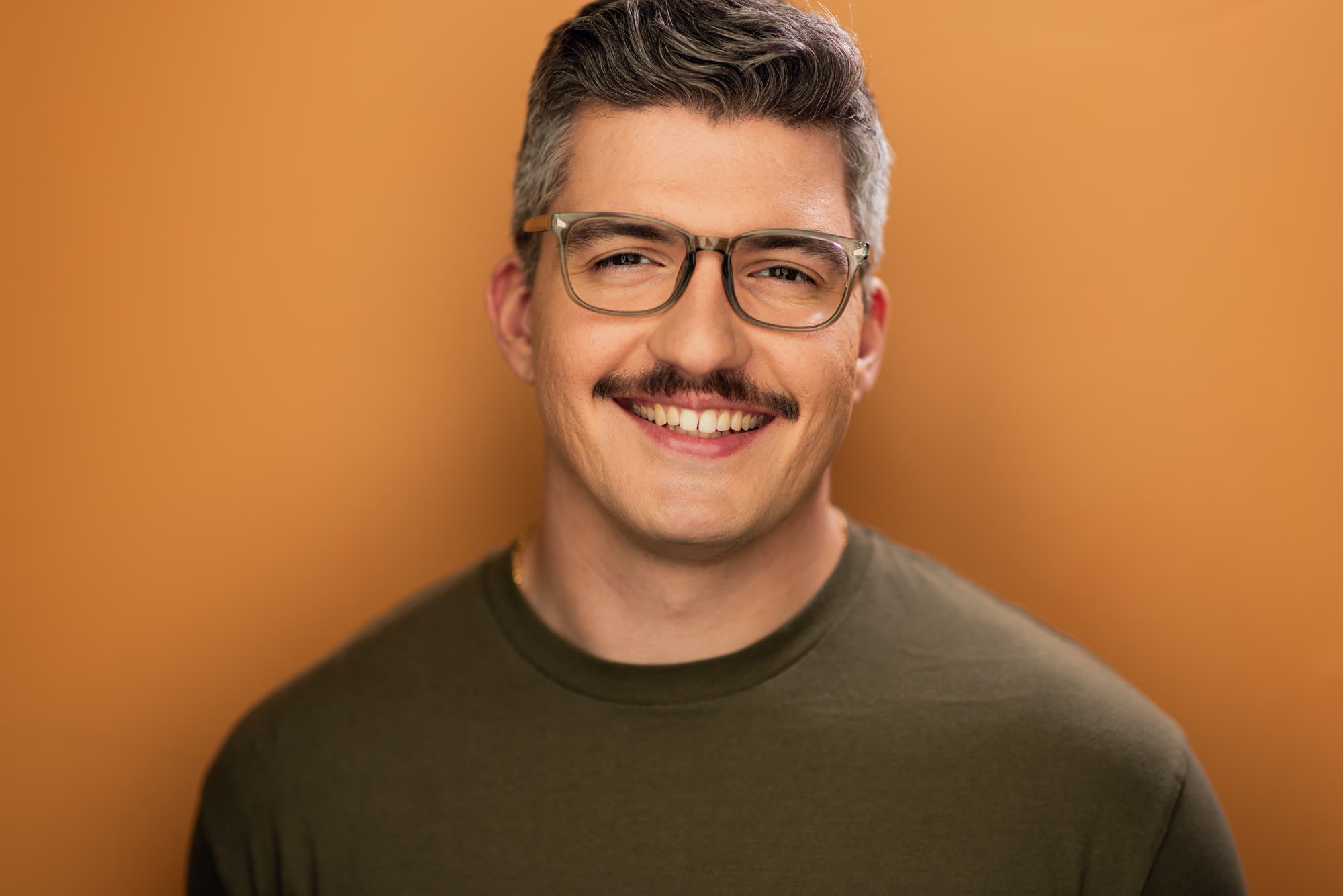 Eugene Romanchuk, commercial headshot: smiling, olive t-shirt against an orange background